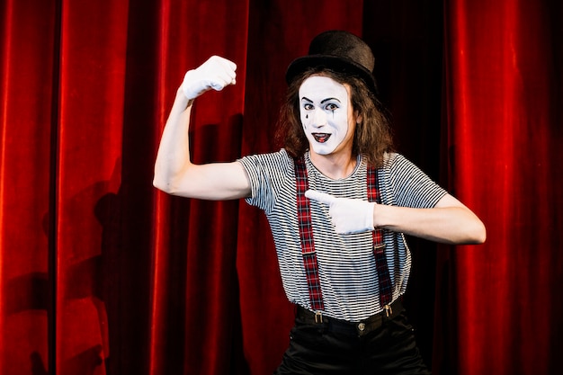 Smiling male mime pointing finger toward flexing muscle