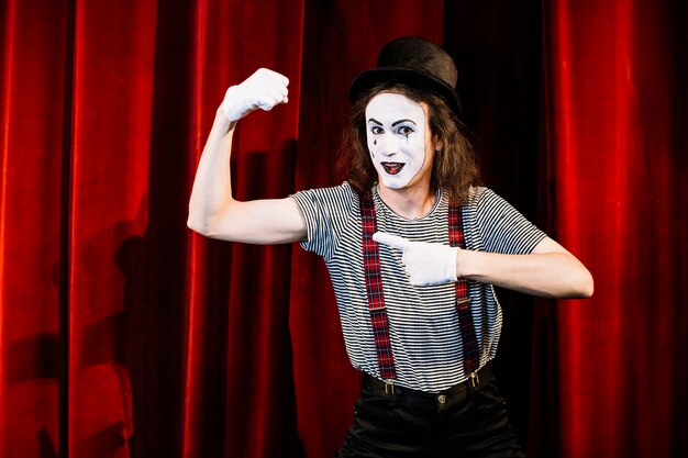 Smiling male mime pointing finger toward flexing muscle