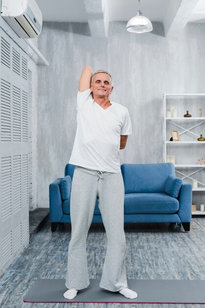 Smiling male pensioner doing stretching exercise in front of sofa at home