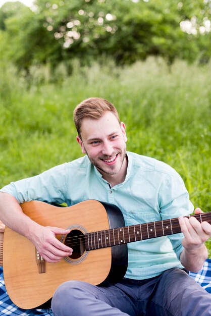 ピクニックにギターを弾く男性の笑みを浮かべてください。