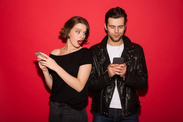 Smiling male punk using smartphone while woman peeps at him