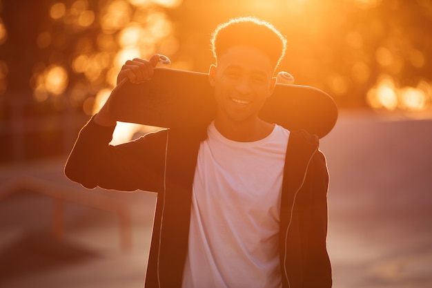 Smiling male teenager guy holding skateboard on shoulders