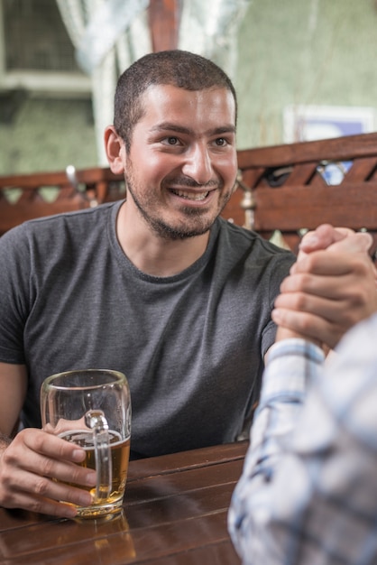 Smiling man arm wrestling with friend in bar