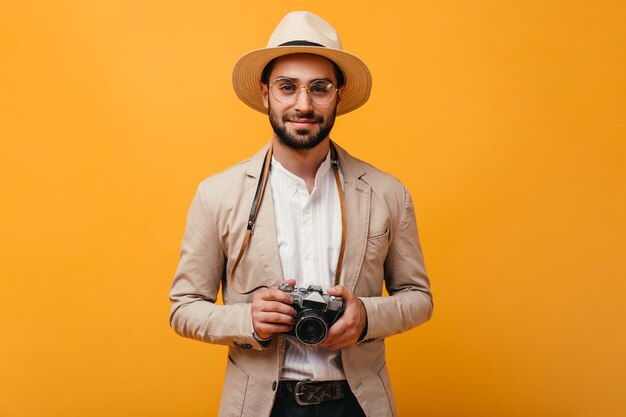 Smiling man in beige outfit holding retro camera on orange wall