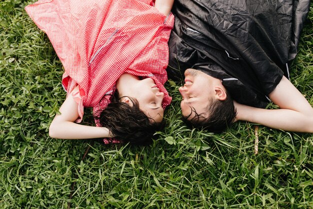 地面に横たわっている黒いレインコートの笑顔の男。幸せそうな表情で草の上でポーズをとる疲れた若者たち。