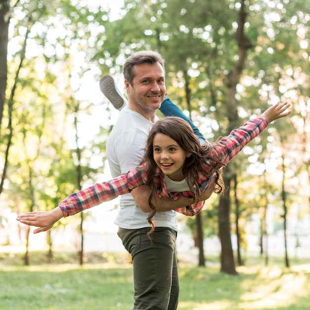 Smiling man carrying his cute daughter in park