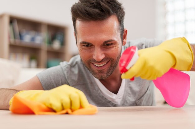 Smiling man cleaning desk in living room