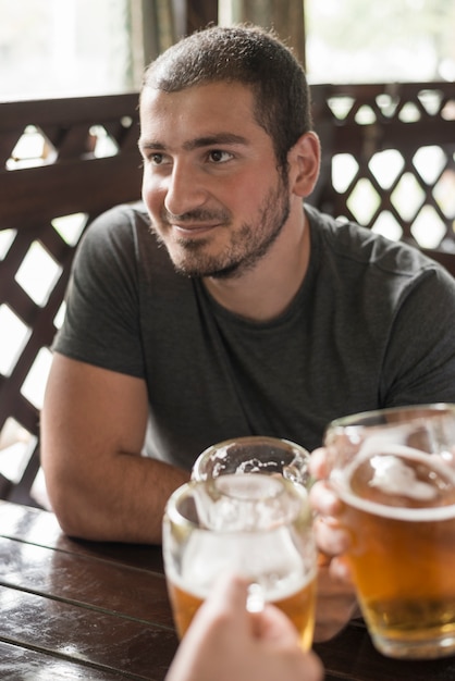 Smiling man drinking beer with friends at pub table