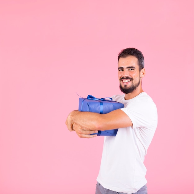 Scatola di regalo d'abbraccio sorridente dell'uomo che sta contro il contesto rosa