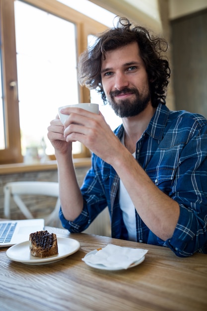 Smiling man having coffee and pastry in coffee shop