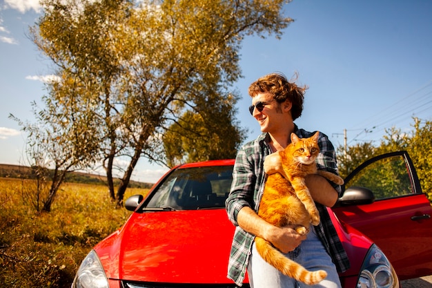 무료 사진 차 앞에서 고양이 들고 웃는 남자