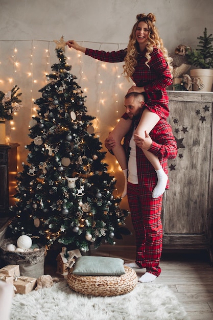 Улыбающийся мужчина держит красивую жену на плечах в канун Рождества