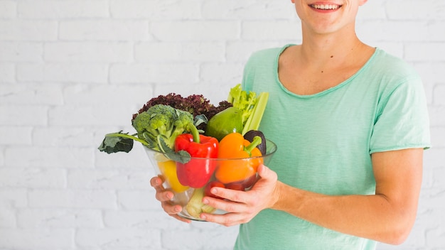 Foto gratuita ciotola sorridente della holding dell'uomo di verdure organiche fresche