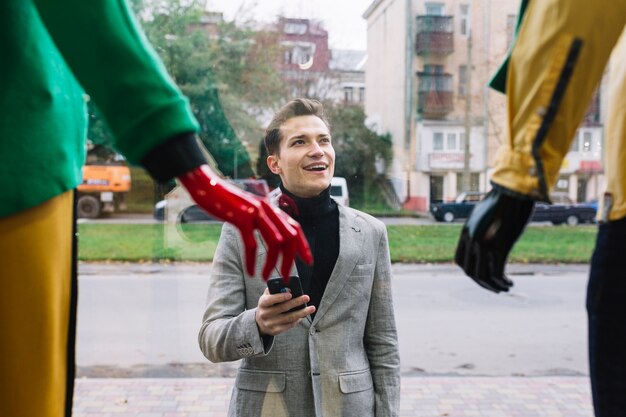 Smiling man holding cell phone looking at window display