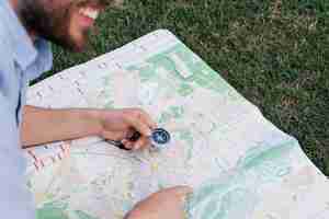 Free photo smiling man holding compass and pointing at map on grass