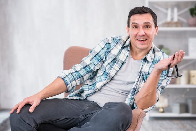 Free photo smiling man holding eyeglasses on chair at home