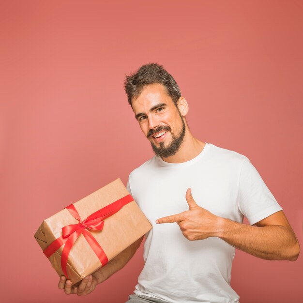 Улыбаясь мужчина держит подарочную коробку указывая пальцем на цветной фон