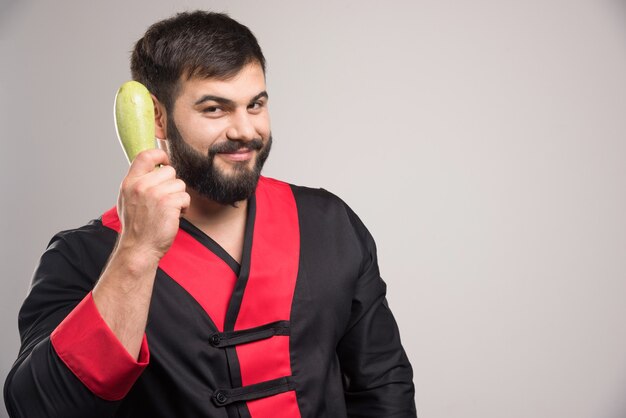 Smiling man holding in hand fresh zucchini .