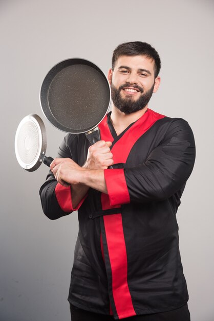 2つの暗い鍋を手に持っている笑顔の男。