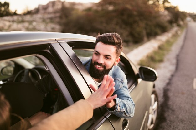 Smiling man holding hands with his girlfriend outside of car