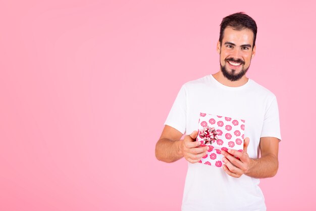 Foto gratuita uomo sorridente che tiene il contenitore di regalo floreale rosa contro il contesto rosa