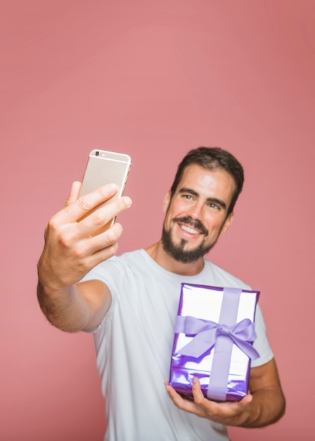 Улыбающийся человек, проведение фиолетовый подарочной коробке, взяв selfie из мобильного телефона