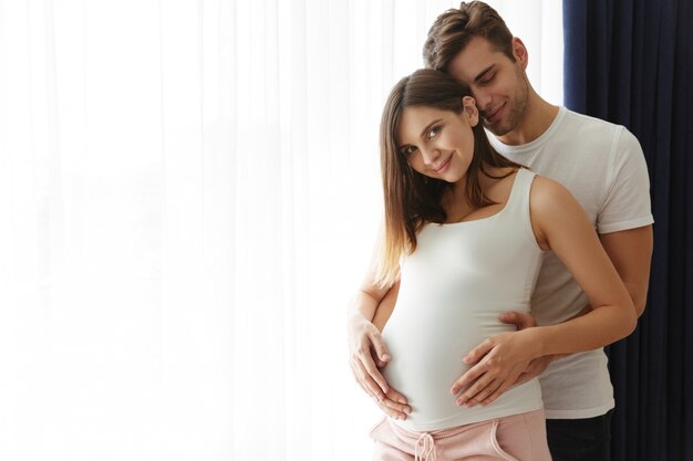 笑みを浮かべて男は自宅で屋内で彼の素敵な妊娠中の妻を抱擁します。