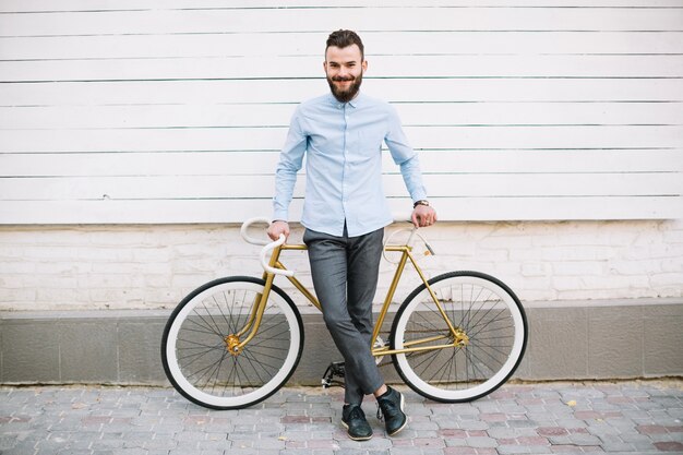 壁の近くの自転車に傾いている笑顔の男