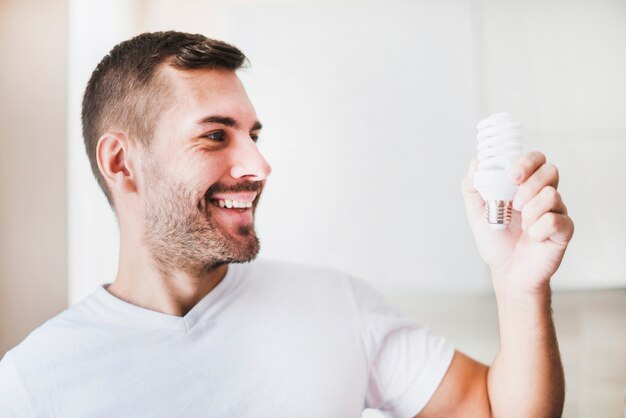Smiling man looking at compact fluorescent light bulb