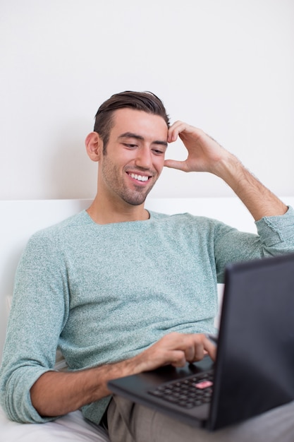 Smiling Man Lying on Sofa and Working on Laptop