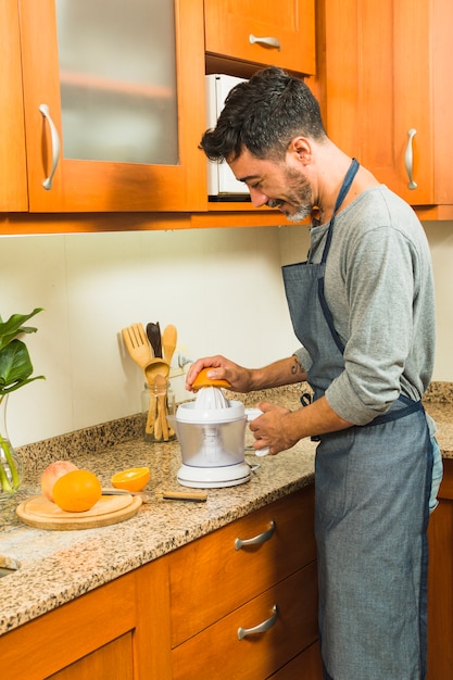 Бесплатное фото Улыбающийся человек делает апельсиновый сок с помощью ручной соковыжималки на кухне
