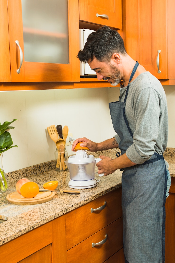 मुफ़्त फोटो smiling man making orange juice using a hand juicer in the kitchen