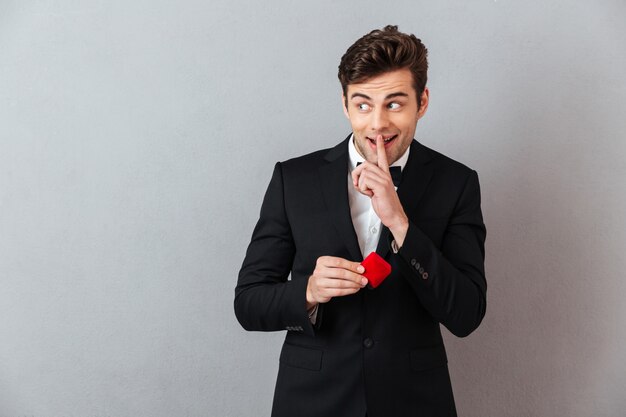 Smiling man in official suit holding box with proposal ring