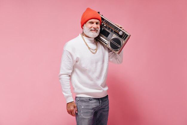 Smiling man in orange hat posing with record player on pink wall