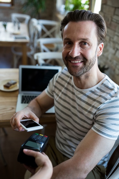 Улыбающийся человек платить с NFC технологии на мобильном телефоне