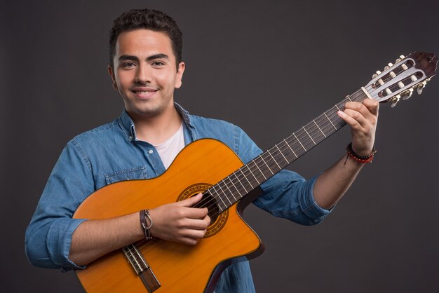 暗い背景でギターを弾く笑顔の男。高品質の写真