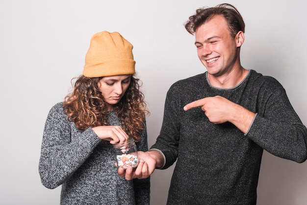 Uomo sorridente che punta il dito alla donna malata che prende le pillole dalla mano