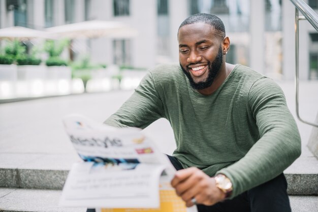 Smiling man reading newspaper on stairs