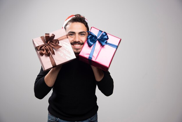 新年の贈り物を持っているサンタの帽子をかぶった笑顔の男。