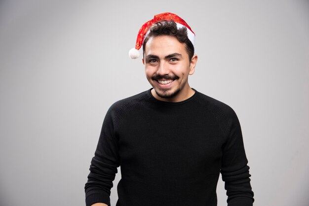 회색 벽 위에 서있는 산타의 빨간 모자에 웃는 남자.