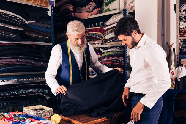 Smiling man seller displaying blue fabrics to young customer in textile shop