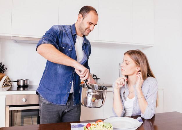 Улыбающийся человек подает еду своей жене на кухне