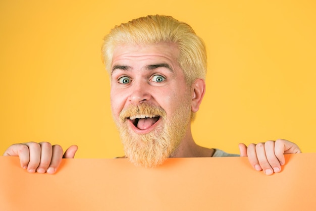 Smiling man showing blank yellow board over blue background