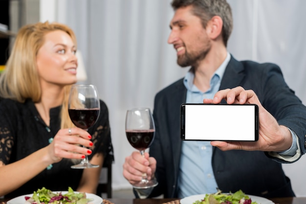 Smiling man showing smartphone near woman with glasses of wine 