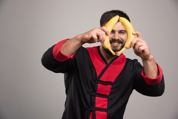 Free photo smiling man showing two bananas on dark surface.