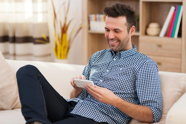 Smiling man sitting on coach and using smart phone