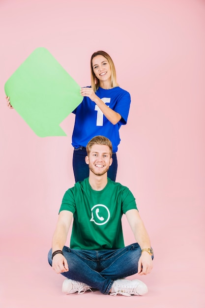 Smiling man sitting in front of woman holding empty green speech bubble