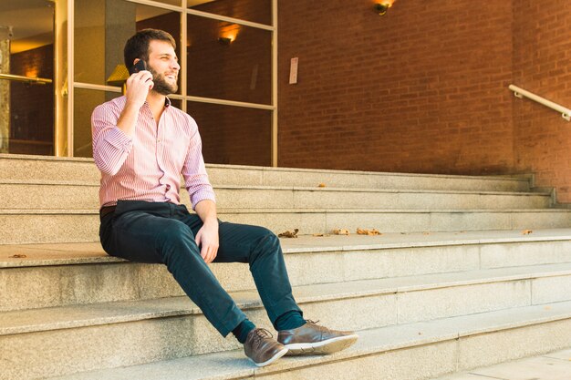 Smiling man sitting on staircase talking on mobile phone