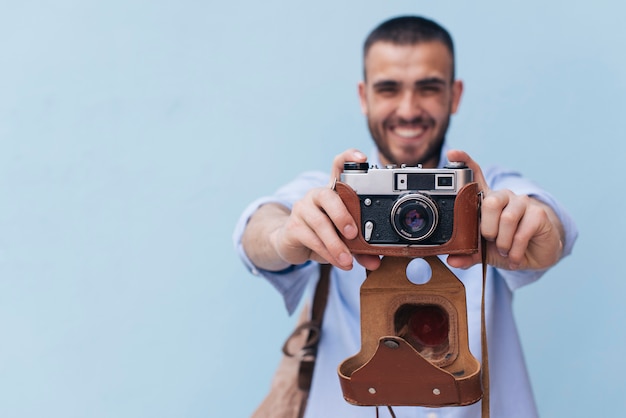 Free photo smiling man taking photo with retro camera standing against blue wall