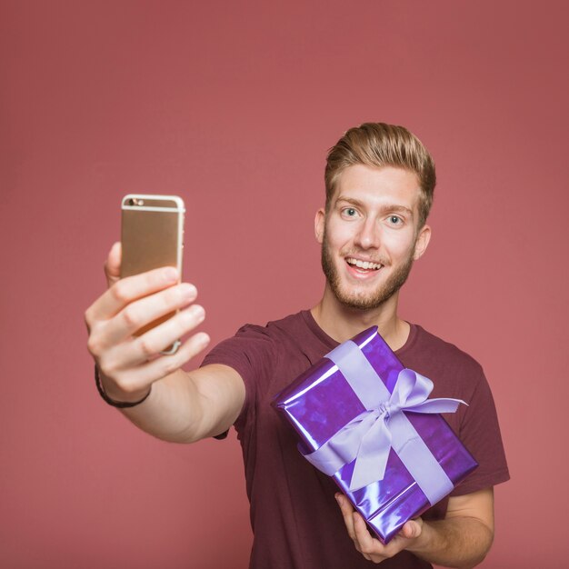 Smiling man taking self portrait from mobile holding gift box